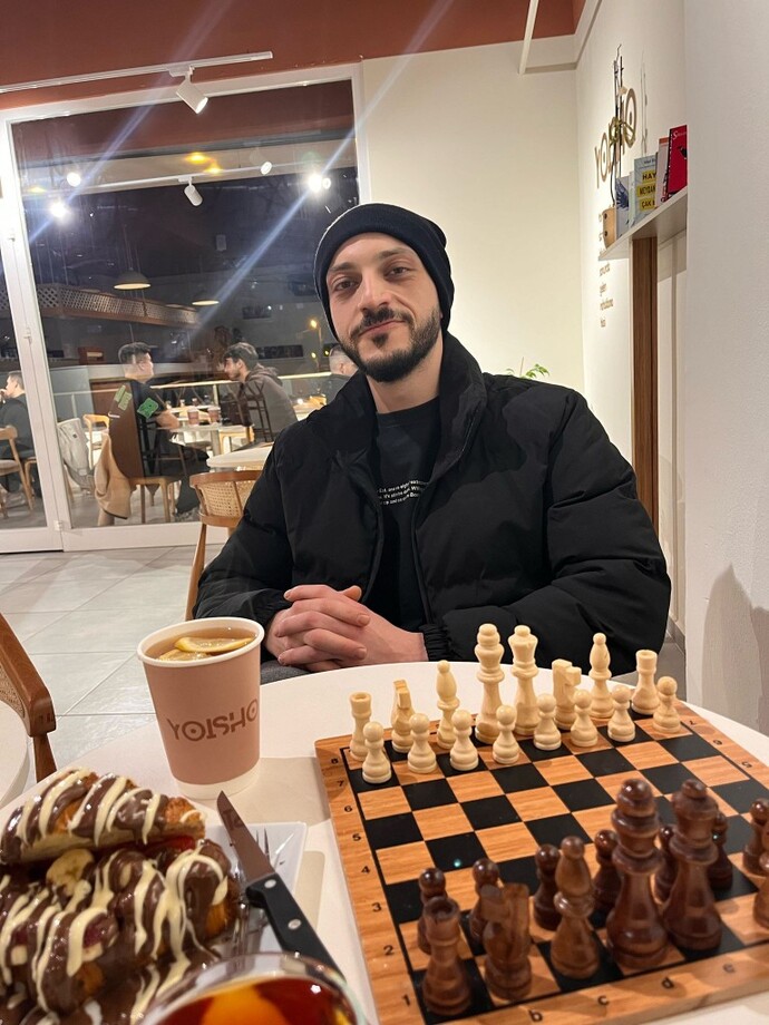 Masasında satranç takımı , çay ve waffle olan kapşonlu bir erkek neden bu kadar tatlıdır?