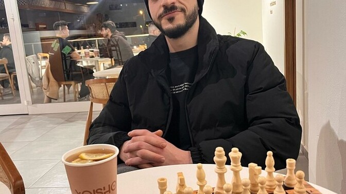 Masasında satranç takımı , çay ve waffle olan kapşonlu bir erkek neden bu kadar tatlıdır?